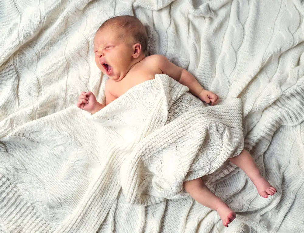 Very tired baby yawning in bed