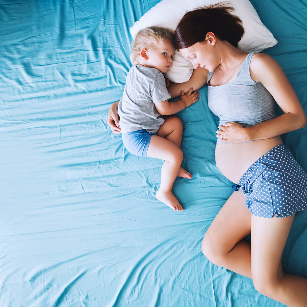 Pregnant mum expecting her second baby lying in bed with toddler