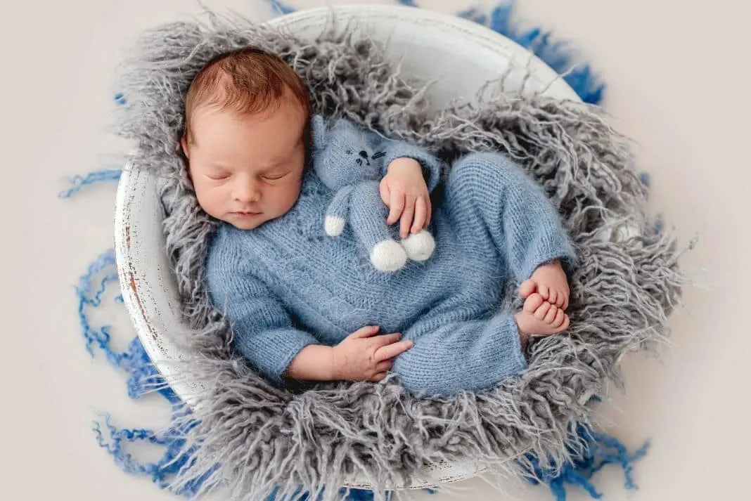 Baby boy in blue knitted outfit asleep in basket